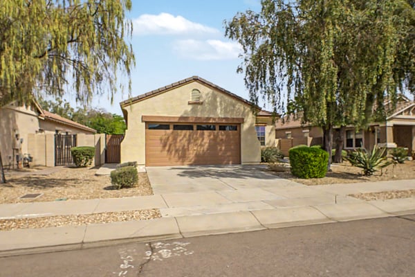 Front exterior highlighting the attached 2-car garage, spacious driveway, mature landscaping, and attractive curb appeal that enhances this move-in-ready Goodyear home.