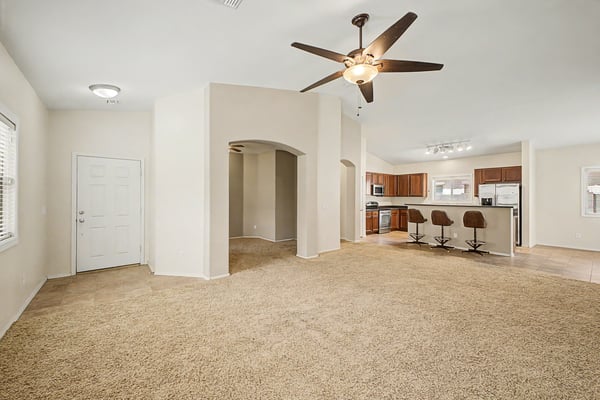 Spacious open great room with soaring vaulted ceilings, plush carpet, and direct views into the kitchen, offering an inviting layout for gatherings and everyday comfort.