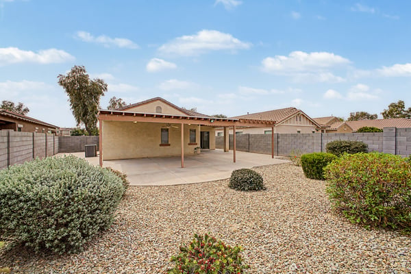 Low-maintenance backyard with attractive desert landscaping, mature plantings, block fencing, and a spacious covered patio, offering privacy and easy outdoor enjoyment in Goodyear.