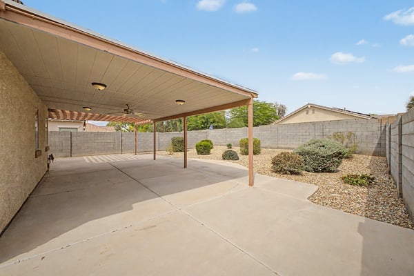 Large covered patio with ceiling fan, extended concrete surface, and views of the beautifully landscaped backyard, providing comfortable outdoor living space in this Goodyear home.