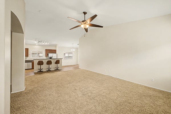 Comfortable living room featuring vaulted ceilings, ceiling fan, plush carpeting, and an open floor plan that enhances the home's bright and airy atmosphere.