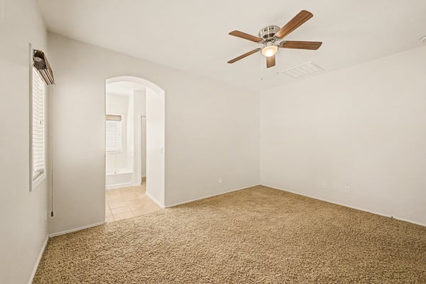 Peaceful primary bedroom offering soft carpeting, ceiling fan, and convenient access to the ensuite bath, providing comfort and privacy.