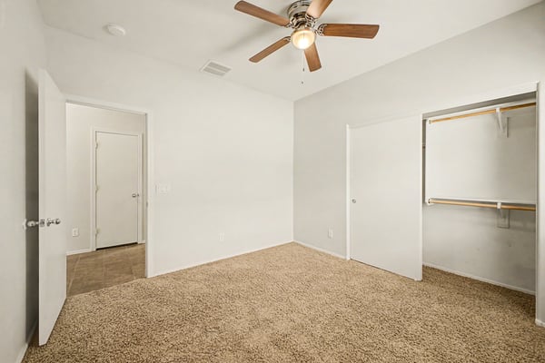 Bright guest bedroom with ceiling fan, neutral d cor, plush carpeting, and generous closet space, ideal as a bedroom, office, or hobby room.