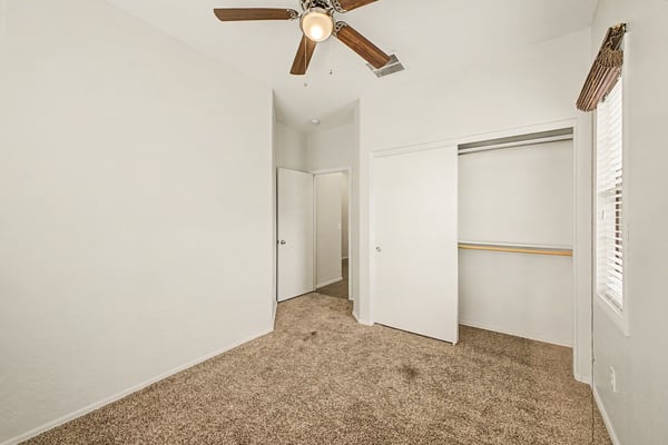 Inviting secondary bedroom with neutral finishes, ceiling fan, plush carpeting, and a roomy closet, providing flexible space for guests, family, or a home office.
