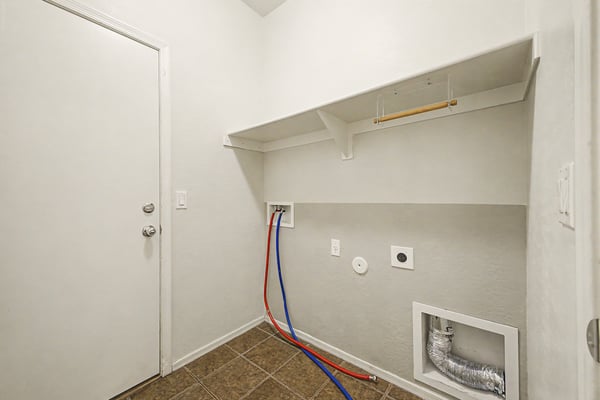 Spacious laundry room featuring tile flooring, washer and dryer connections, built-in shelving, and exterior access for added convenience and organization.