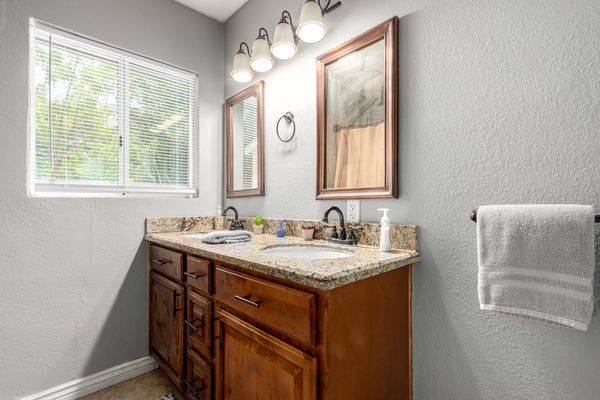 Updated guest bathroom with granite countertops, wood cabinetry, modern lighting, and generous vanity storage. A functional and attractive space designed for everyday living.