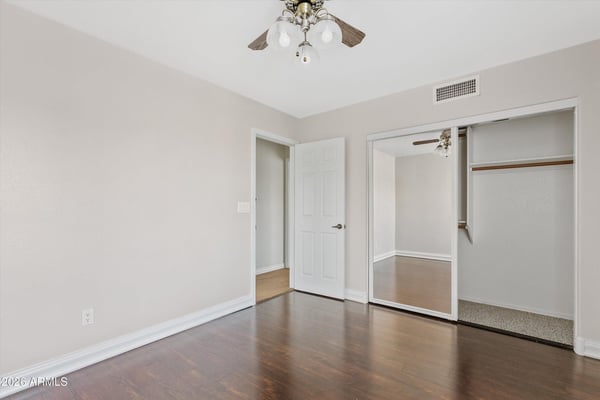 Featuring rich wood flooring, mirrored closet doors, and a ceiling fan, this spacious bedroom provides comfort, storage, and flexibility for guests or family members.