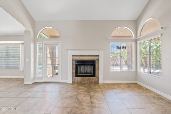This welcoming family room features a wood-burning fireplace, soaring ceilings, and French doors leading to the covered patio. The spacious layout creates a comfortable gathering place with easy indoor-outdoor flow.