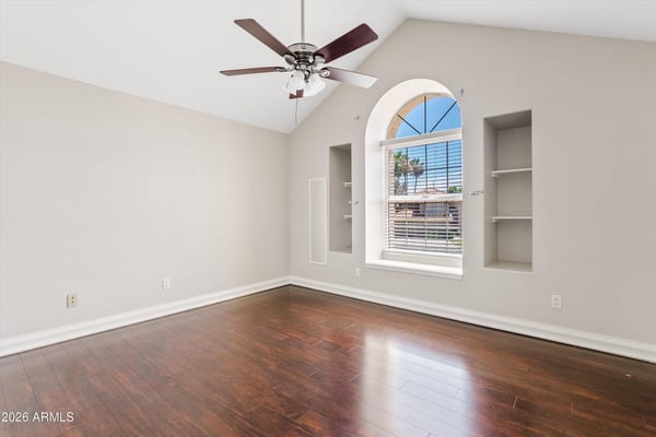 Soaring vaulted ceilings, decorative wall niches, wood flooring, and an elegant arched window create a bright and welcoming bedroom filled with natural light.