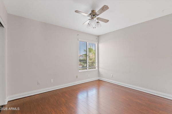 Large windows bring abundant natural light into this inviting bedroom featuring wood flooring, neutral finishes, and a ceiling fan. A comfortable space that complements this Chandler home.