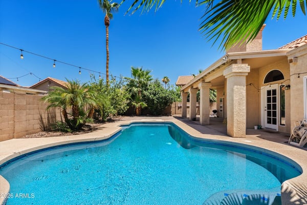 A sparkling swimming pool, mature tropical landscaping, expansive covered patio, and inviting outdoor spaces combine to create a backyard designed for year-round enjoyment in Chandler.