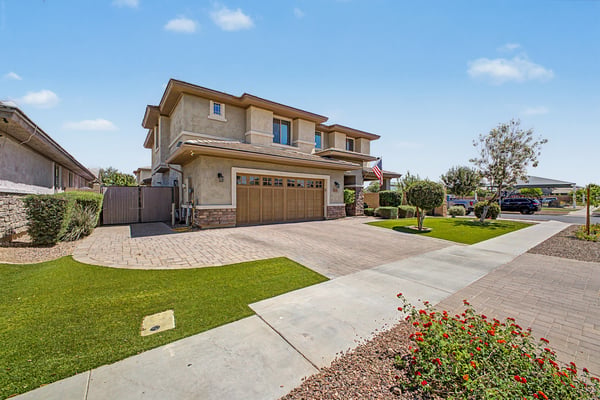 Exterior view highlighting the extended paver driveway, lush landscaping, covered front porch, and attached 3-car garage, creating outstanding curb appeal in Morrison Ranch.