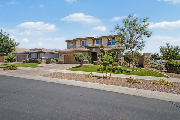 Beautifully landscaped front yard with mature trees, manicured greenery, stone accents, and timeless architecture that enhances the charm and appeal of this Mesa home.