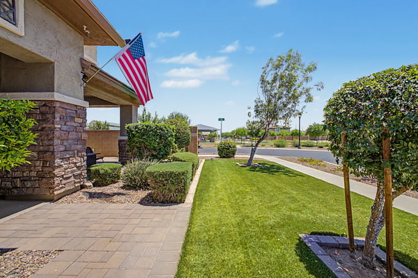 Professionally landscaped front yard with green lawn, mature trees, paver walkway, and inviting curb appeal enhances the beauty of this exceptional Morrison Ranch home in Mesa.