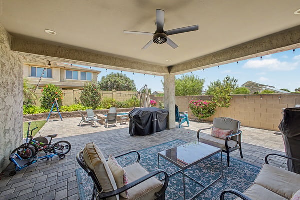 Covered backyard patio features paver hardscaping, ceiling fan, landscaped yard, and multiple seating areas, creating an inviting outdoor space for relaxing and entertaining in Mesa.