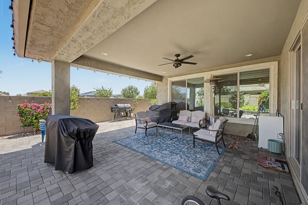 Large covered patio offers paver flooring, ceiling fan, multiple seating areas, and outdoor entertaining space that extends the living area into the beautifully landscaped backyard.