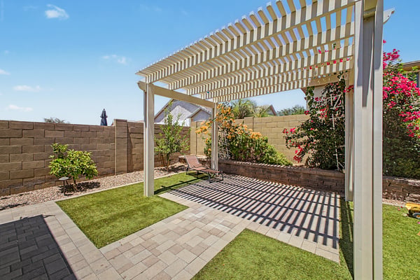 Pergola-covered outdoor space offers filtered shade, artificial turf, mature landscaping, and flexible space for lounging, reading, or enjoying Mesa's beautiful weather.