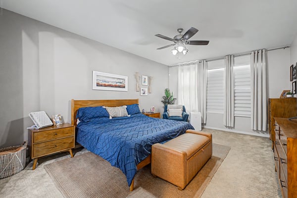 Spacious owner's suite offers plush carpeting, plantation shutters, neutral colors, and room for additional seating, creating a comfortable and inviting private retreat.
