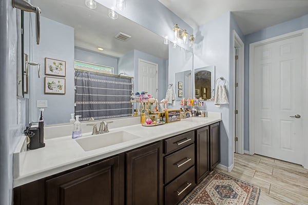 Stylish bathroom showcases a dual-sink vanity with quartz countertops, modern cabinetry, updated lighting, and generous storage for everyday convenience.