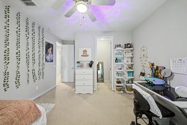 This spacious bedroom includes room for both sleeping and studying, featuring neutral finishes, ceiling fan, plush carpeting, and flexible living space.