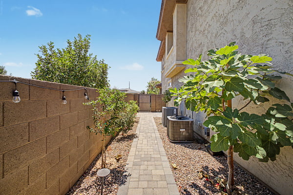 Functional side yard features a paved walkway, mature landscaping, low-maintenance desert design, and secure gated access for added convenience and ease of maintenance.