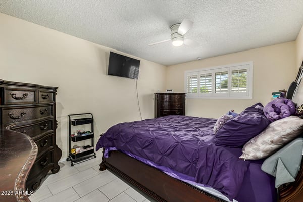 Relaxing primary bedroom featuring tile flooring, plantation shutters, ceiling fan, generous proportions, and abundant natural light for year-round comfort.