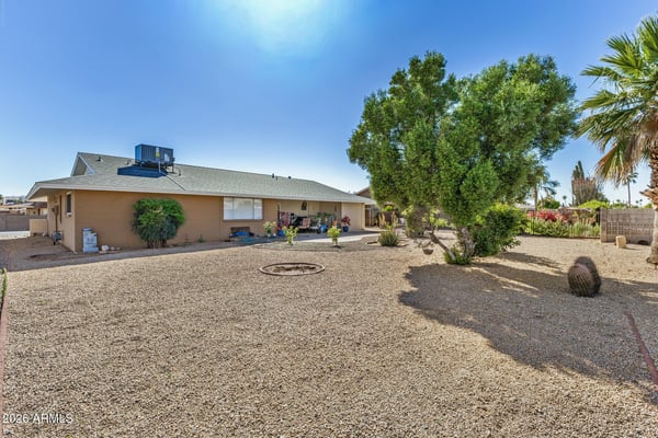 Expansive backyard with mature trees, gravel landscaping, and open outdoor areas offers endless possibilities for entertaining, gardening, or peaceful relaxation in Sun City.