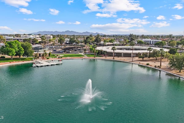 Wide aerial view showcases the community lake, decorative fountain, recreation center, marina, and surrounding neighborhood. Experience the scenic lifestyle available in Sun City.