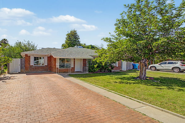 Attractive Phoenix home featuring classic brick architecture, an oversized paver driveway, mature landscaping, and a covered entry that creates exceptional curb appeal and a welcoming first impression.