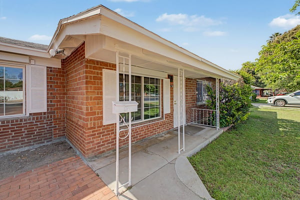 Charming covered front porch with brick accents, security entry, and large picture windows overlooking the landscaped front yard, creating a warm welcome to this Phoenix property.
