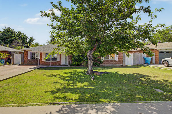 Full front exterior featuring a mature shade tree, lush green lawn, brick construction, and inviting front walkway. This Phoenix home offers timeless curb appeal and attractive outdoor space.