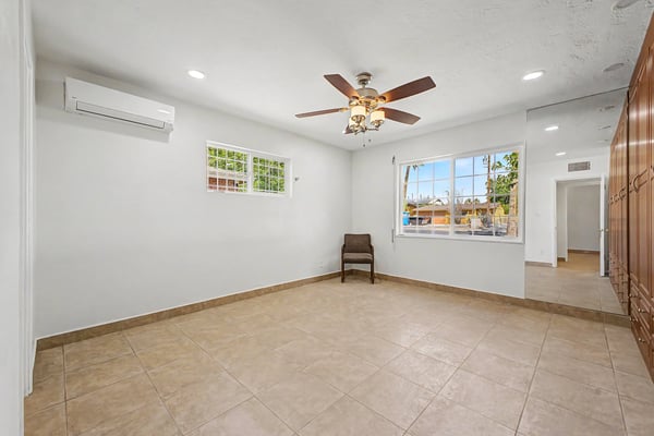 Spacious owner's bedroom featuring custom built-in wardrobes, tile flooring, ceiling fan, split-system air conditioning, and oversized windows that fill the room with natural light in this Phoenix home.