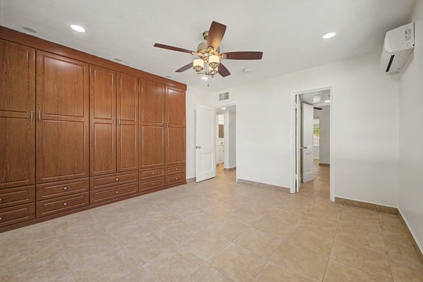 Spacious bedroom offering a full wall of custom built-in wardrobe cabinetry, tile flooring, ceiling fan, recessed lighting, and flexible space ready for your personal design.