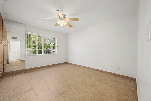 Bright secondary bedroom featuring tile flooring, ceiling fan, custom built-in storage, large picture window, and a comfortable layout with abundant natural light in this Phoenix home.