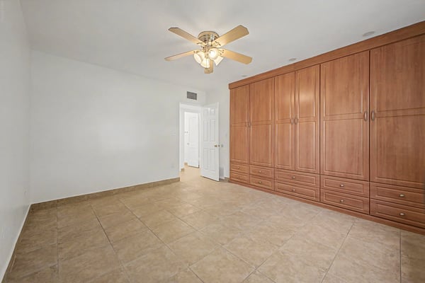 Spacious bedroom showcasing custom built-in wardrobe cabinetry, durable tile flooring, ceiling fan, and an open layout with abundant natural light. This versatile room easily accommodates guests, family, or a home office in this Phoenix property.