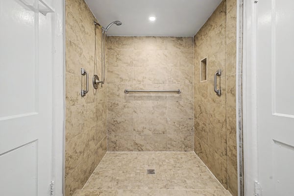 Beautifully tiled walk-in shower featuring grab bars, recessed storage niche, handheld showerhead, and modern finishes. Designed for comfort and convenience, this upgraded bathroom enhances the home's appeal.