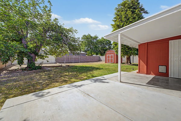 Covered patio opens to a spacious backyard featuring mature shade trees, grassy lawn, and a detached storage shed. A wonderful outdoor setting for entertaining, relaxing, or everyday enjoyment in this Phoenix home.