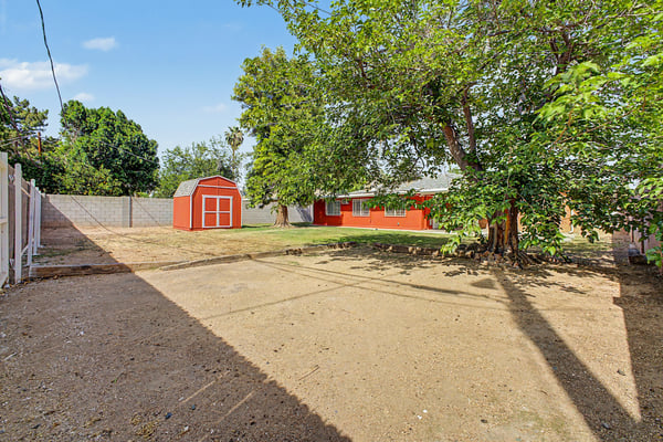 Backyard view highlighting mature trees, detached storage shed, and generous open space ready for landscaping, recreation, or entertaining. The spacious yard adds valuable flexibility to this Phoenix home.