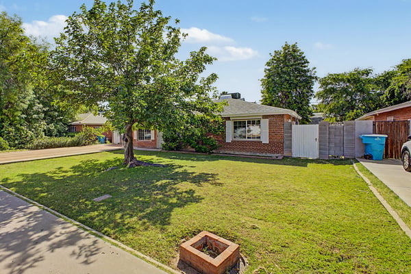 Attractive front view showcasing mature landscaping, brick accents, gated side yard access, and a spacious lawn. This well-kept exterior reflects the pride of ownership throughout this Phoenix property.