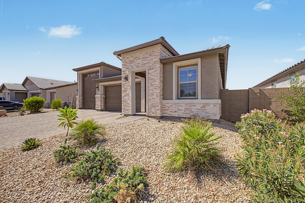 Covered front entry framed by elegant stonework welcomes guests with timeless style. Desert landscaping and quality exterior finishes create lasting curb appeal.
