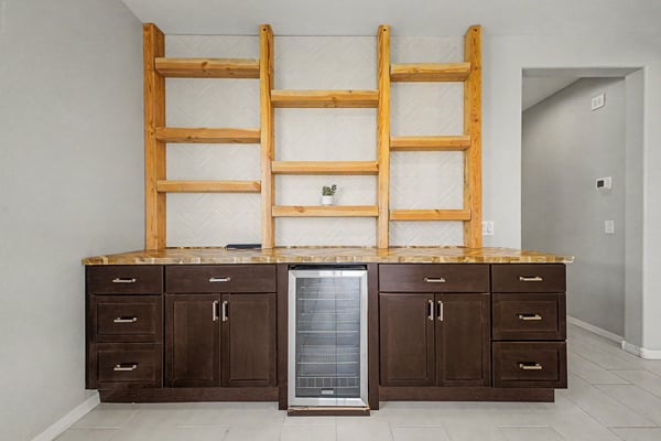 Custom cabinetry with rich wood shelving and integrated beverage refrigerator provides elegant storage and display space, making this bonus area both beautiful and functional.