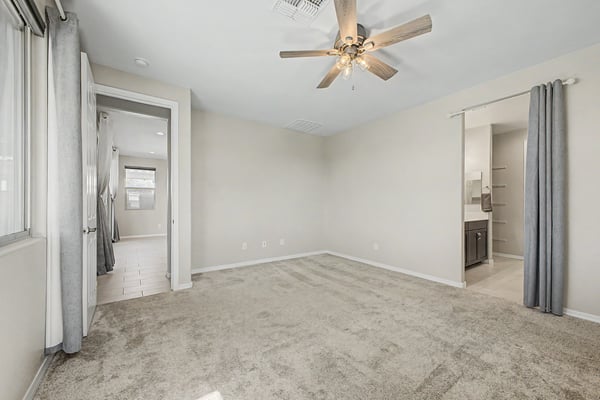 Generously sized primary bedroom with soft carpeting, neutral tones, ceiling fan, and convenient access to the walk-in closet and ensuite bath. A peaceful space to begin and end each day.