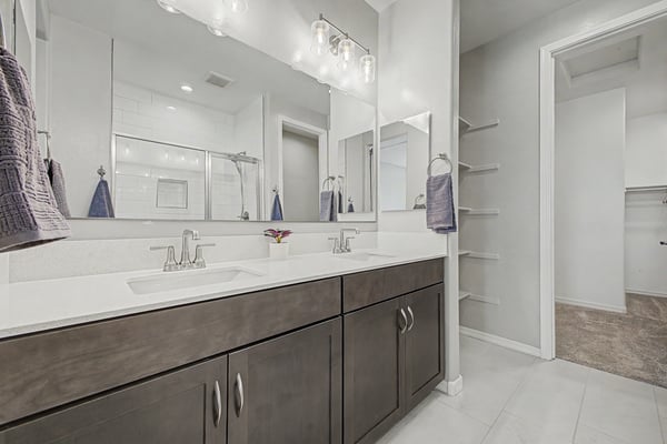 Spacious primary bathroom with dual quartz vanities, contemporary lighting, oversized mirrors, built-in storage shelves, and convenient access to the walk-in closet. Blending elegance with everyday functionality.