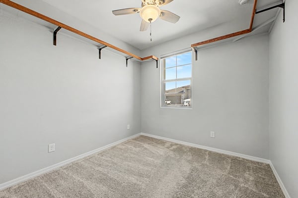 Bright secondary bedroom with plush carpeting, ceiling fan, custom open shelving, and a large window. Perfect as a guest room, home office, or hobby space in this beautiful Wittman residence.