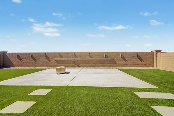 Spacious outdoor entertaining area with artificial turf, a large concrete patio surrounding the fire pit, decorative wall feature, and plenty of room for outdoor furniture and gatherings.
