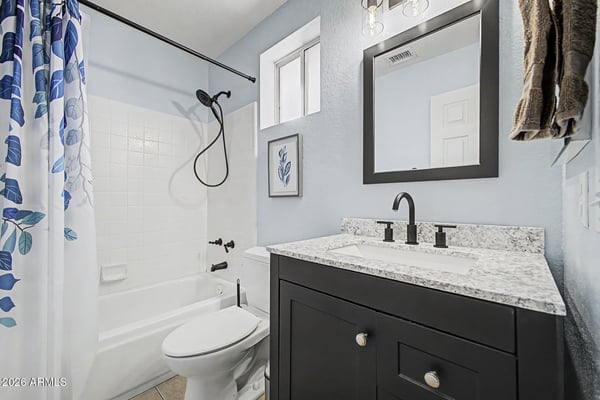The renovated hall bathroom showcases granite countertops, updated cabinetry, modern black fixtures, stylish lighting, and a tub/shower combination, offering both functionality and contemporary appeal.