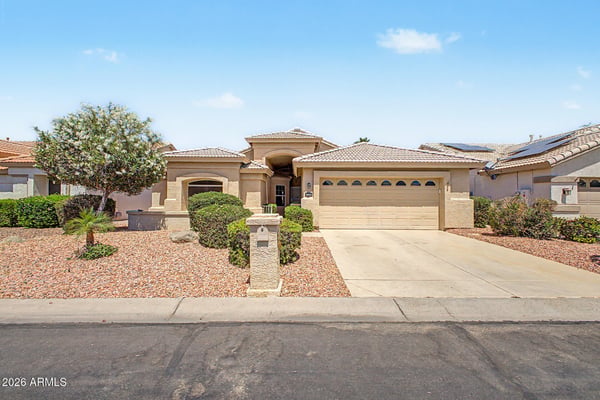 A charming front elevation showcases mature landscaping, a covered entry, spacious driveway, and attached two-car garage. This beautifully maintained Goodyear rental offers excellent curb appeal without being located on a corner lot.