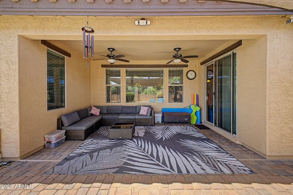 Enjoy year-round outdoor comfort beneath the covered patio complete with ceiling fans, comfortable seating, sliding glass door access, and views of the beautifully landscaped backyard in Goodyear.