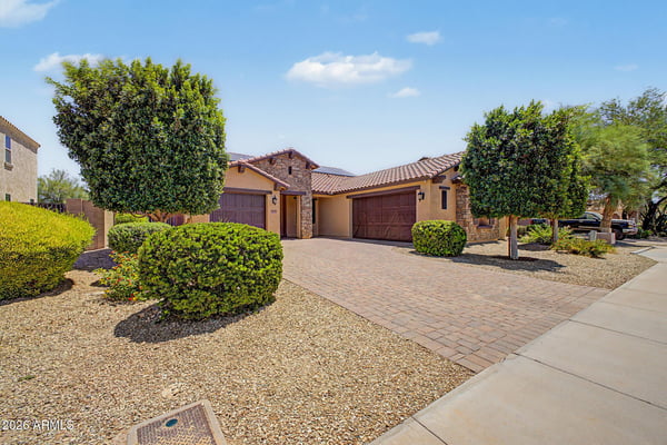 A broad front exterior view highlights the stone-accented elevation, paver driveway, mature landscaping, and welcoming curb appeal of this beautifully maintained rental property in Goodyear.
