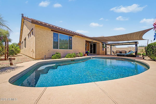 Enjoy resort-style outdoor living with a sparkling pool, covered entertaining area, shade sail, paver patio, and low-maintenance landscaping that make this Goodyear rental ideal for relaxing year-round.